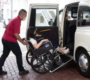 A man in a wheelchair is being assisted into a van by a caregiver.