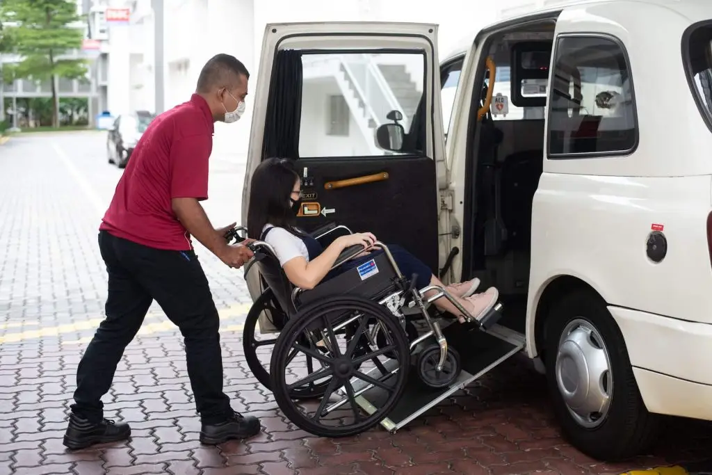 A man in a wheelchair is being assisted into a van by a caregiver.